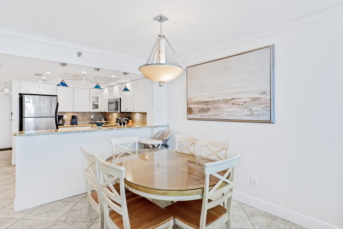 Your stylish dining space flows seamlessly into a fully-equipped kitchen, where coastal artwork creates a serene backdrop for memorable meals together.