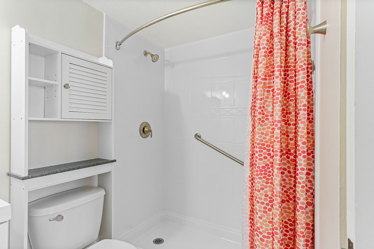 Step into your bright, accessible bathroom featuring a spacious walk-in shower with safety grab bars and cheerful coral-patterned curtain.