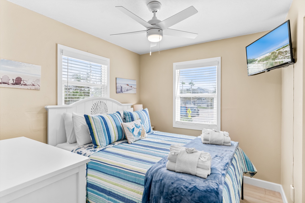 Drift into peaceful sleep in your coastal-themed bedroom, complete with soft blue linens, ceiling fan comfort, and beach artwork.