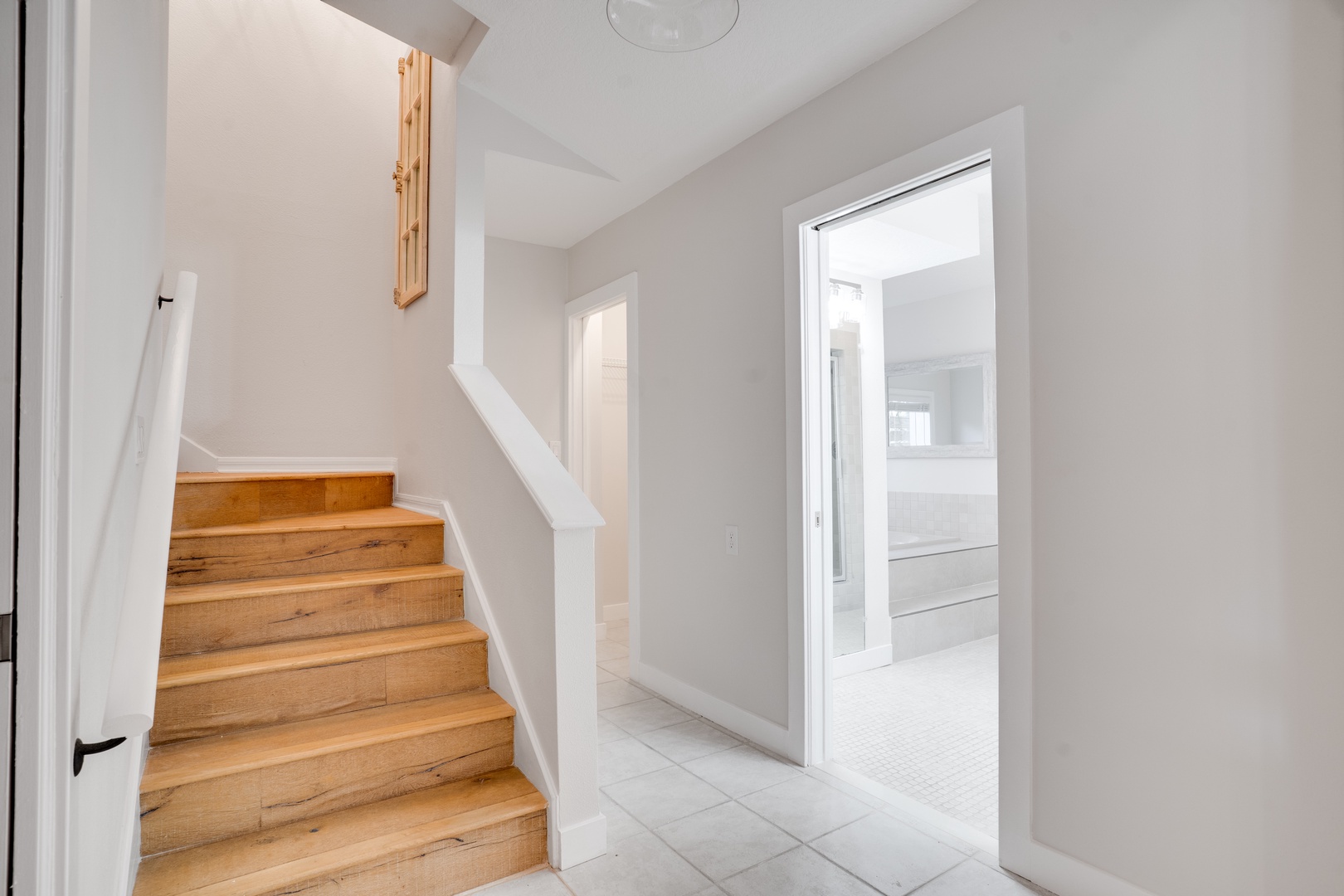 Step into your bright, modern entryway where warm wood stairs and pristine white walls create an inviting welcome home.