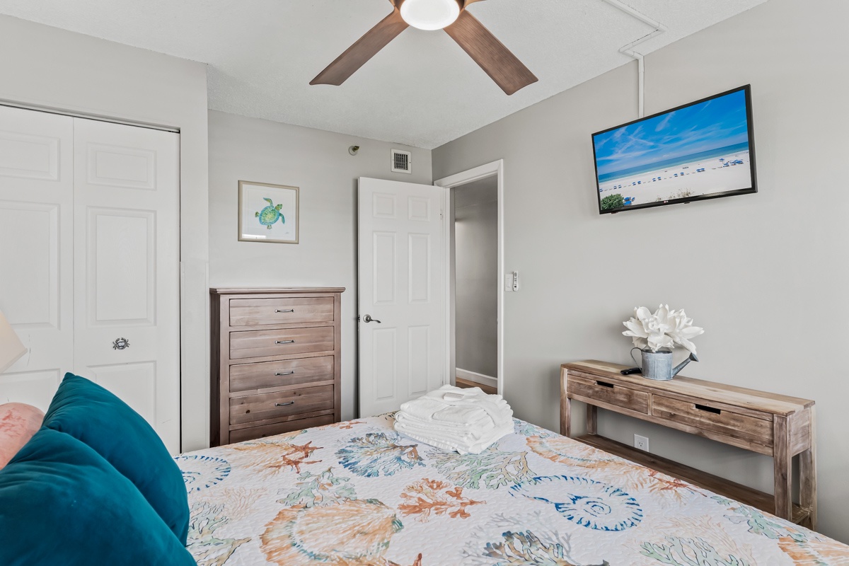 Settle into this bright, coastal-inspired bedroom where soft linens and a gentle ceiling fan promise restful sleep. Your retreat features beach-themed decor and ample storage for all your vacation essentials.