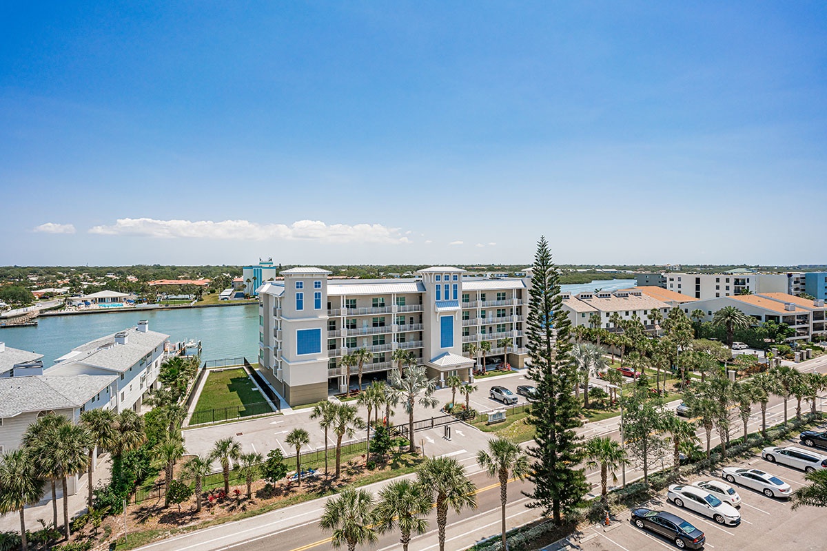 Modern waterfront resort overlooking serene bay waters, surrounded by tropical palms in a peaceful coastal community.