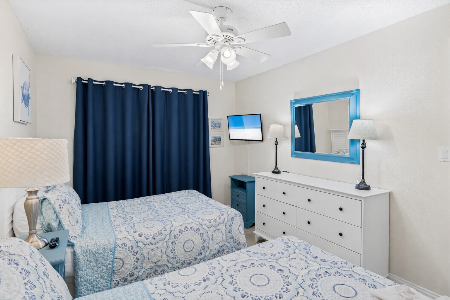 Relax in your bright Queen bedroom with coastal blue accents, ceiling fan, and TV for peaceful evenings after beach adventures.