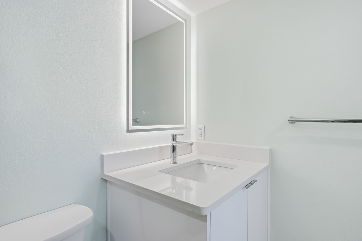 Freshen up in your sleek, modern bathroom featuring crisp white finishes and an illuminated mirror for your daily routines.