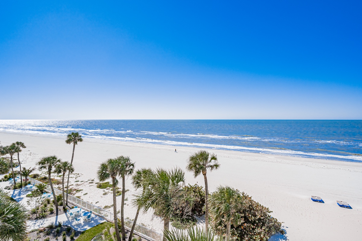 Pristine white sand beach stretches along crystal-clear waters with swaying palm trees and gentle waves rolling ashore.