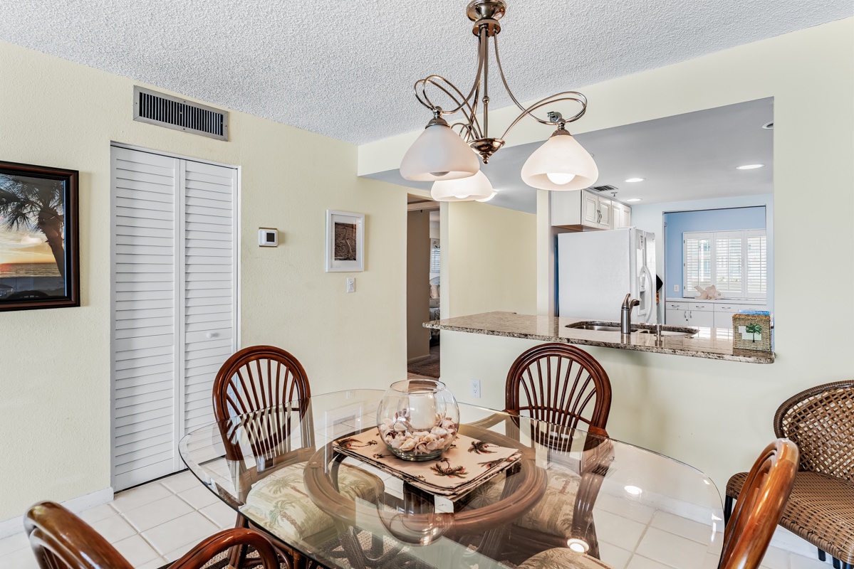 Your dining area flows seamlessly into the kitchen, with a coastal-chic vibe and soft natural light. Gather for meals under the warm glow of the chandelier, with beach decor accents that set the tone for relaxation.