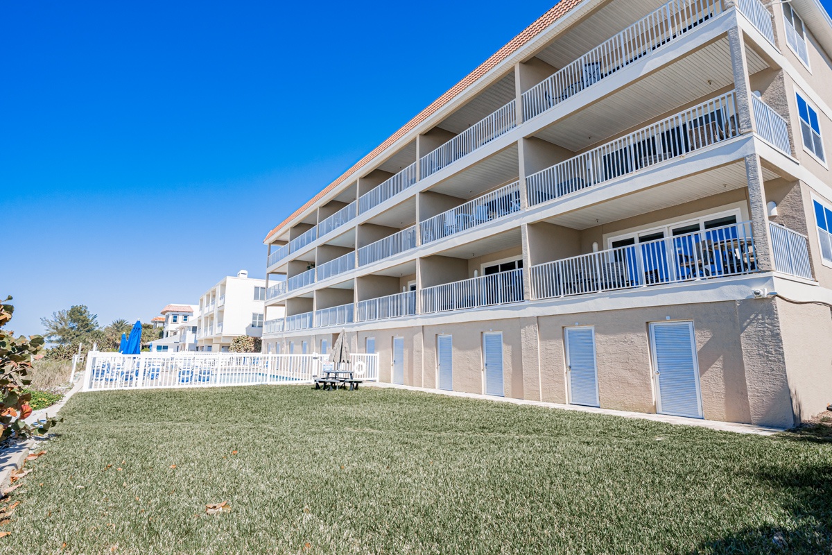 Multi-story beachfront property with private balconies and manicured lawn area overlooking coastal views.