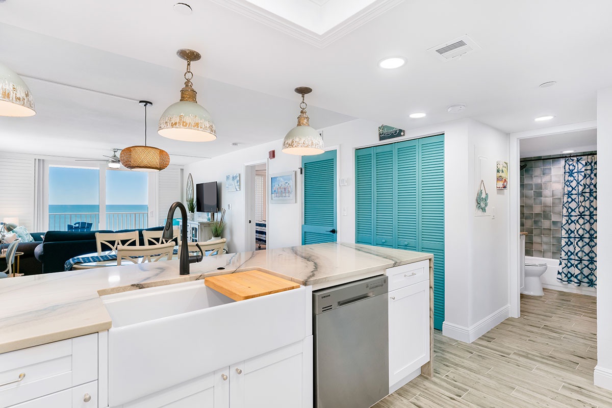 Your bright kitchen flows seamlessly into the living space, where turquoise shutters add coastal charm and ocean views create the perfect backdrop for cooking.