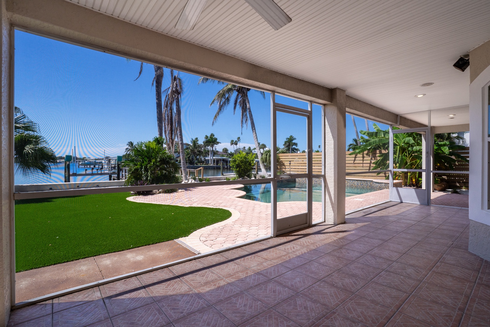 Step into your tropical paradise where floor-to-ceiling glass doors reveal your private pool, lush lawn, and waterfront views.