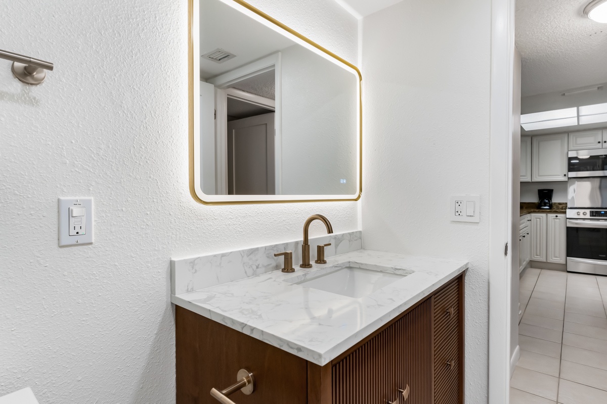 Refresh in your sleek bathroom featuring elegant marble countertops and warm brass fixtures. The backlit mirror and stylish vanity create a sophisticated space where you can start and end your day in comfort.