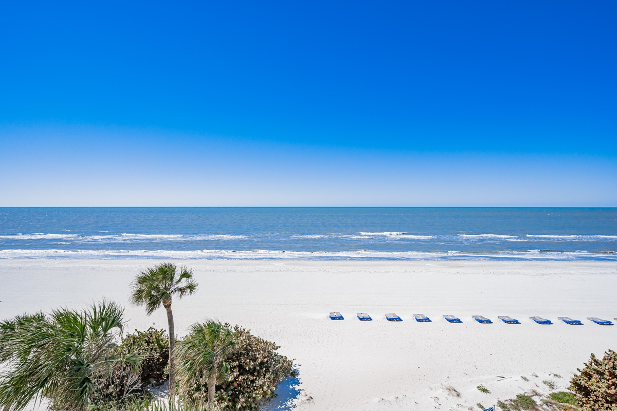 Pristine white sand beach with gentle waves and clear blue skies stretching to the horizon.