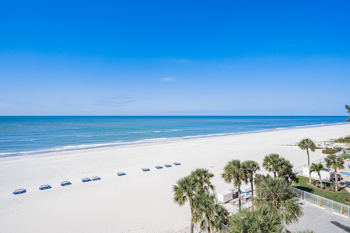 Pristine white sand beach with turquoise waters and swaying palm trees, featuring comfortable beach loungers perfectly positioned for relaxation.