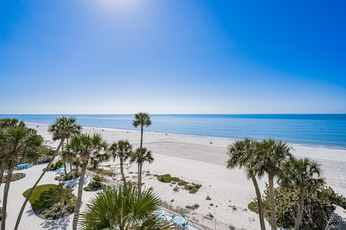 Pristine white sand beach stretches endlessly beneath brilliant blue skies, framed by swaying palms and turquoise waters.