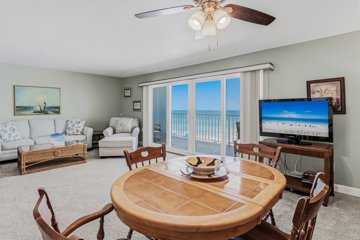 Relax in your bright coastal living space where ocean views await just beyond the glass doors. Enjoy meals at the tiled dining table, unwind on comfortable seating, and let the ceiling fan keep you cool as you soak in the beach vibes.