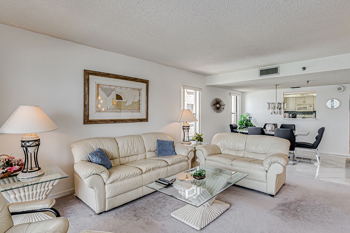 Sink into plush leather sofas in your bright, open living space where glass coffee table reflects natural light streaming through windows.