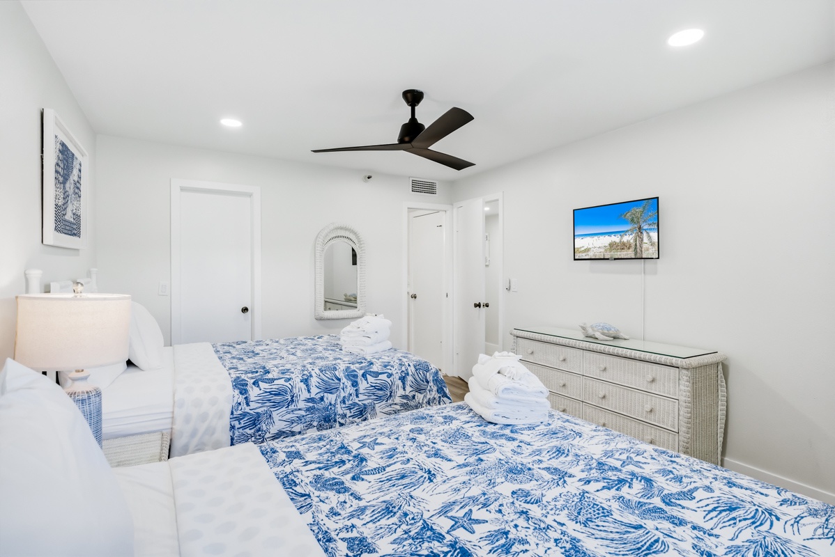 Unwind in your serene bedroom featuring 2 Queen beds with coastal blue linens, modern comfort, and beachside artwork to inspire peaceful dreams.