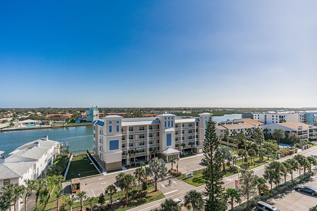 Stunning waterfront development showcasing modern residential buildings nestled along pristine coastal waters with lush palm-lined streets.
