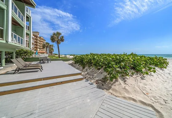 Beachfront property with direct beach access, palm trees, and ocean views under sunny skies.