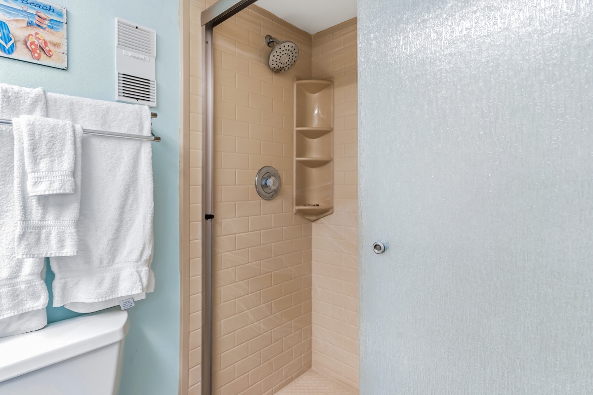Enjoy a refreshing rinse in this clean, tiled walk-in shower with convenient built-in shelving for your toiletries and soft towels waiting for you nearby.