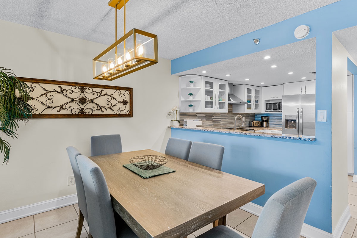 Gather around your stylish dining table, where modern comfort meets coastal charm with ocean-inspired blue accents throughout your open-concept space.