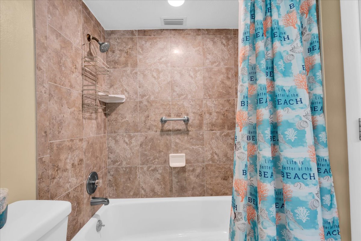 Your private bathroom features warm marble-toned tile, a tub-shower combo with convenient shelving, and a cheerful beach-themed curtain that sets a relaxed coastal mood.