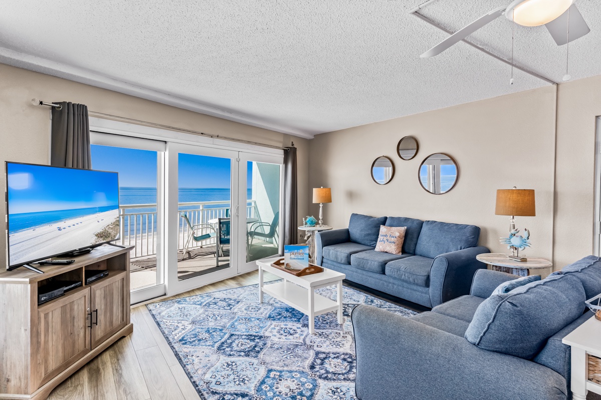 Relax in your oceanfront living room where blue sofas complement stunning sea views through floor-to-ceiling windows, creating your perfect beach getaway.