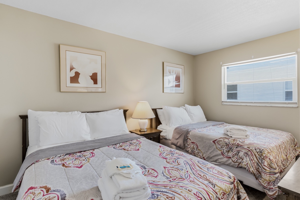 Sink into plush bedding in this serene bedroom, where two inviting beds promise a restful night's sleep. Sunlight filters through the window, warming the space with a gentle glow.