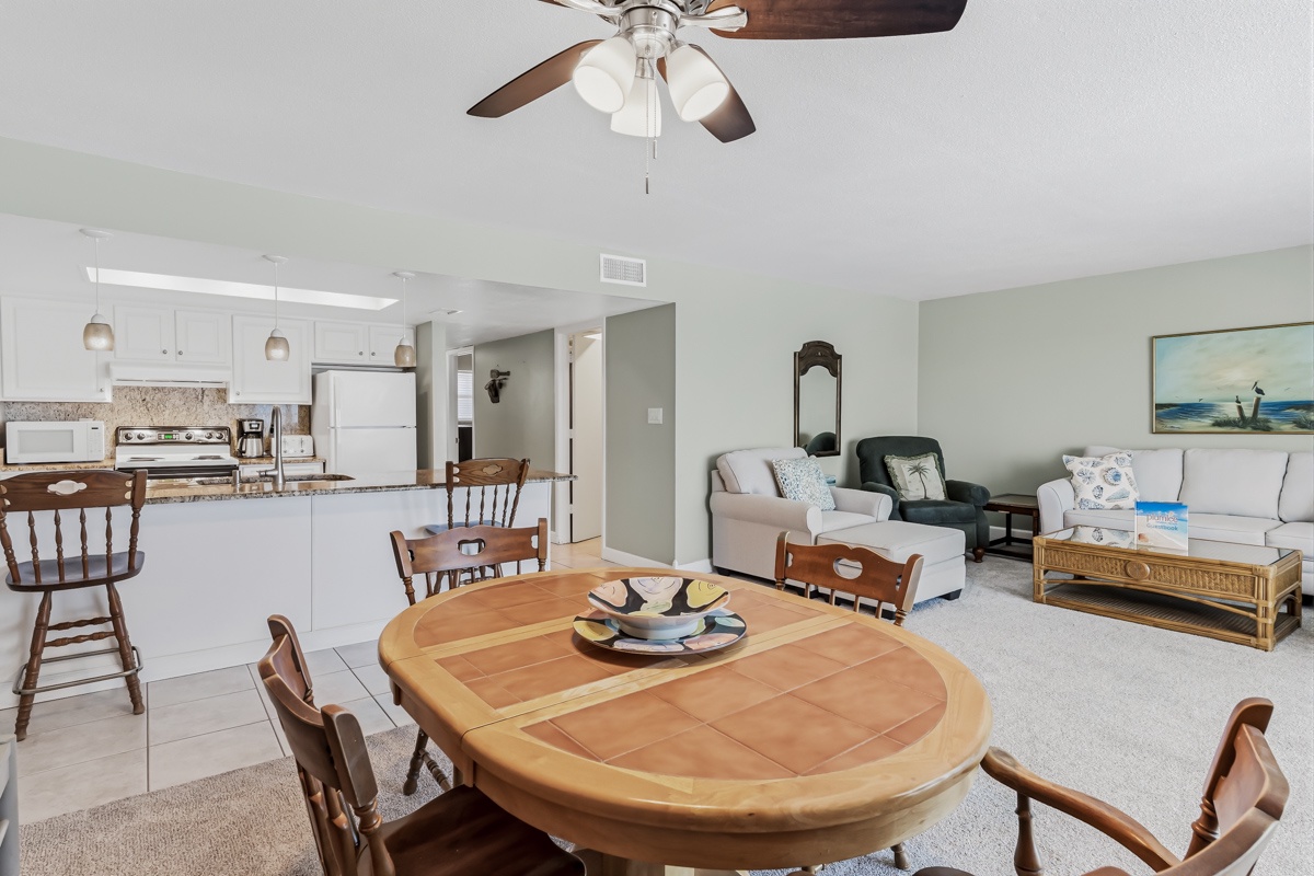 Settle into your open-concept living space where the kitchen, dining, and living areas flow seamlessly together. The soothing coastal palette and gentle ceiling fan breeze create the perfect backdrop for your vacation gathering.
