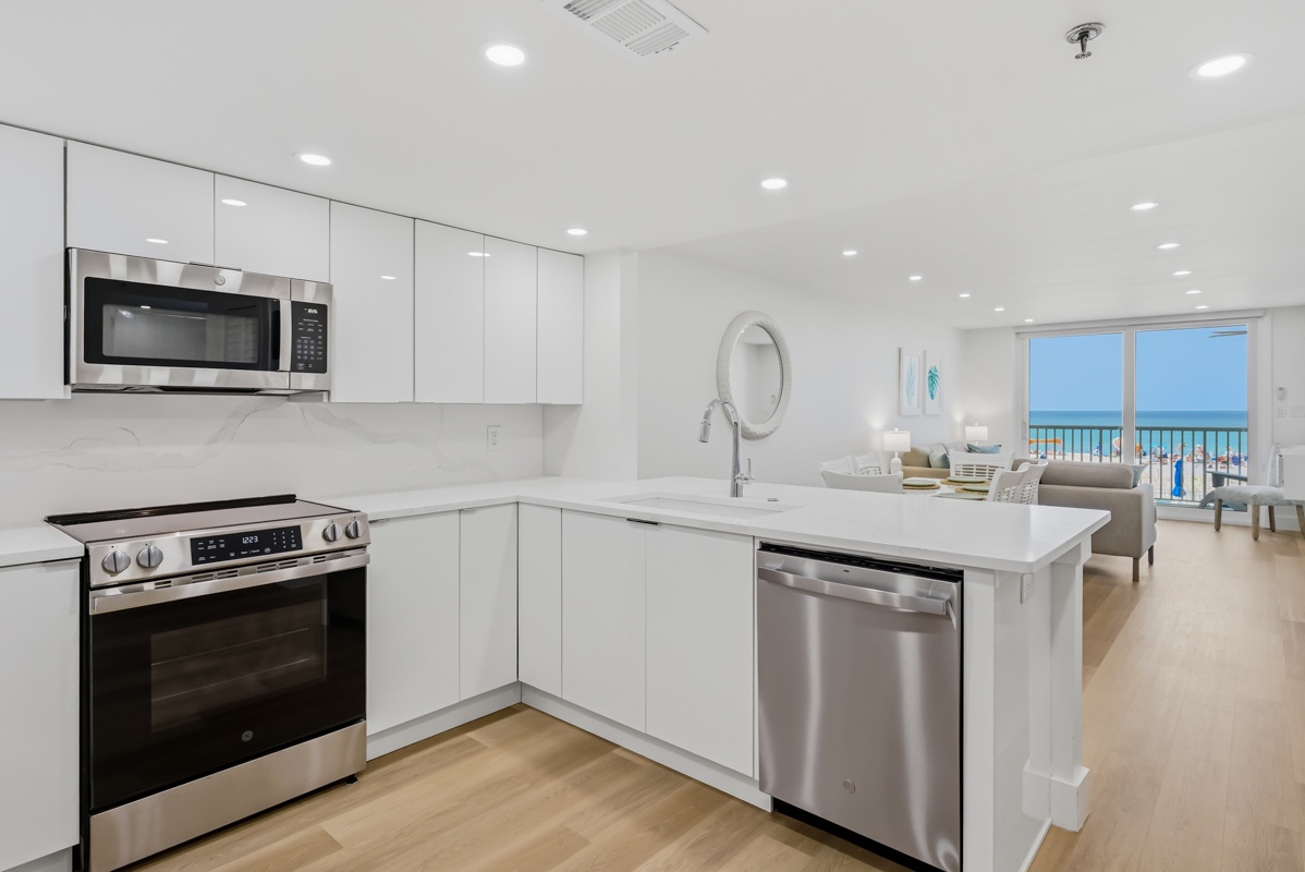 Your stunning ocean-view kitchen features sleek white cabinetry and premium stainless steel appliances, perfect for preparing meals while enjoying breathtaking blue water views.