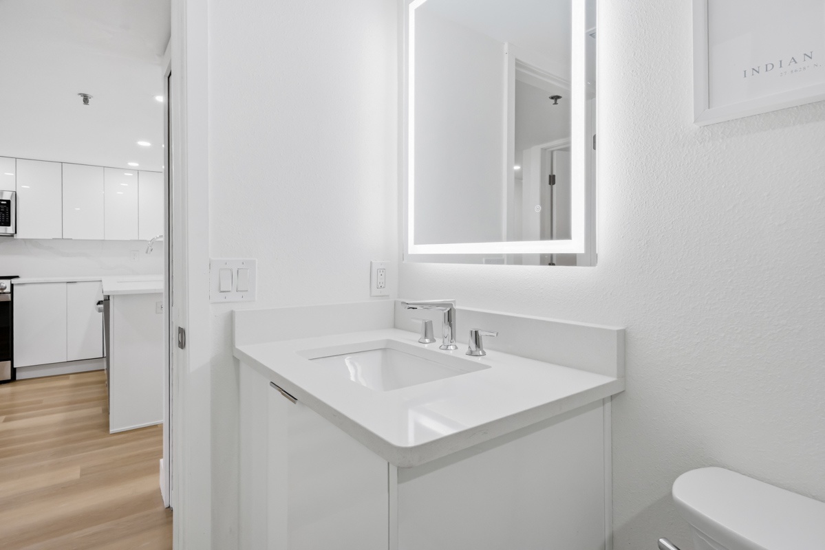 Step into your sleek, modern bathroom featuring pristine white countertops, elegant LED-lit mirror, and contemporary fixtures for your comfort.