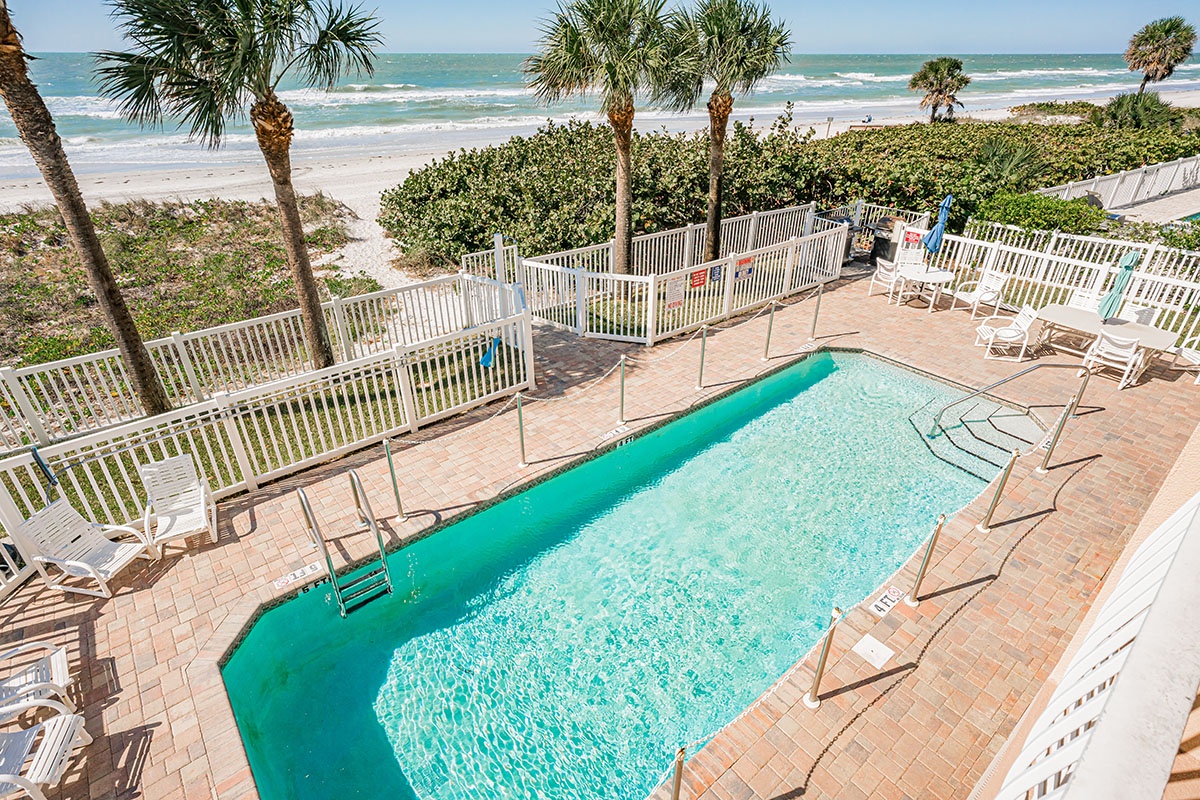Crystal-clear beachfront pool surrounded by palm trees overlooks pristine sandy shores and emerald waters.