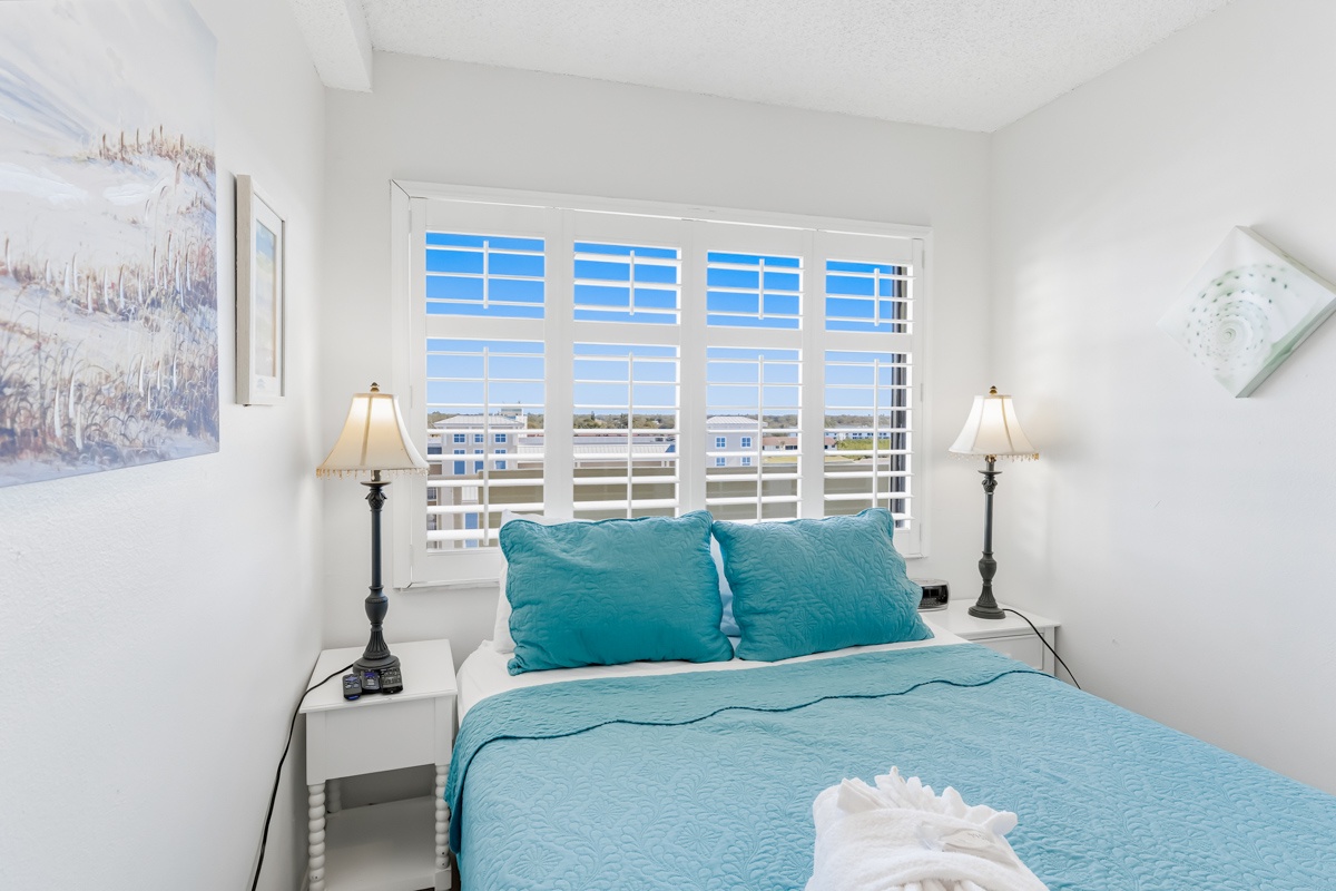 Wake up in your bright bedroom with turquoise linens, plantation shutters, and peaceful city views through expansive windows.