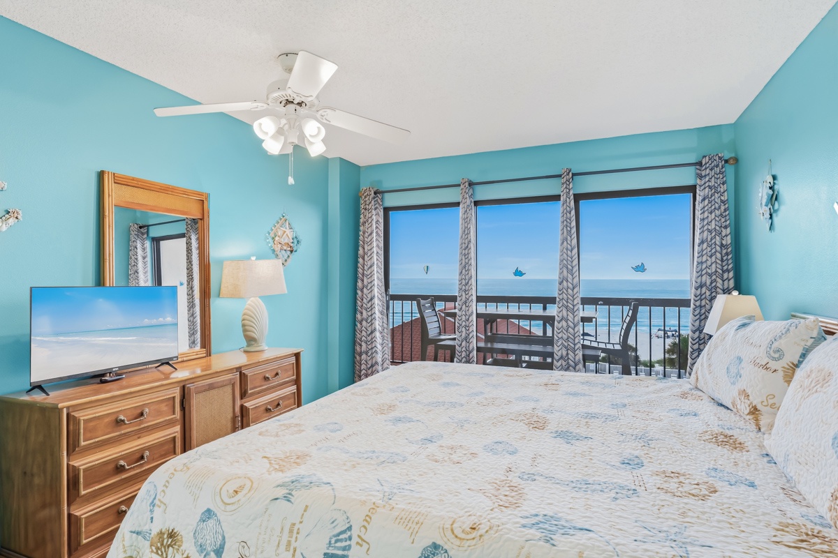 Wake up to stunning sea views from your private balcony. This coastal-themed bedroom offers a peaceful retreat with soothing turquoise tones, a ceiling fan for your comfort, and beachy décor that invites relaxation.