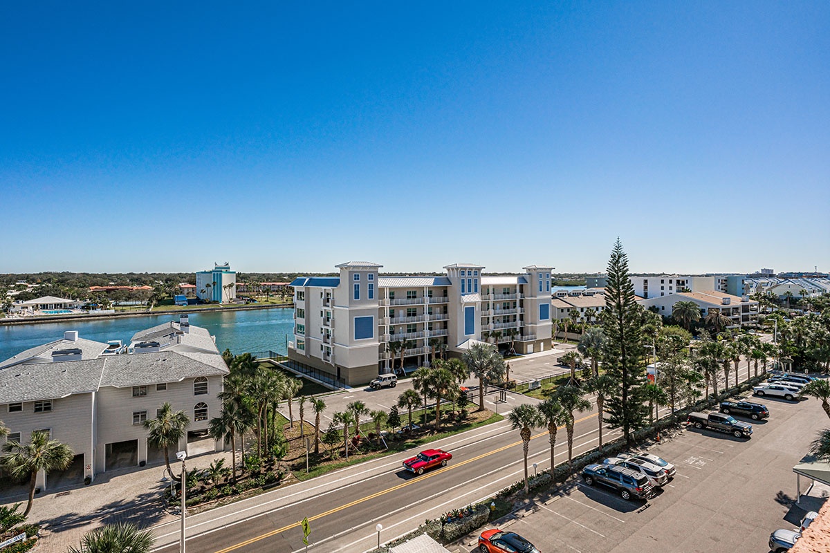 Aerial view of modern waterfront development with multi-story residential buildings, palm-lined streets, and convenient parking areas near the coastline.