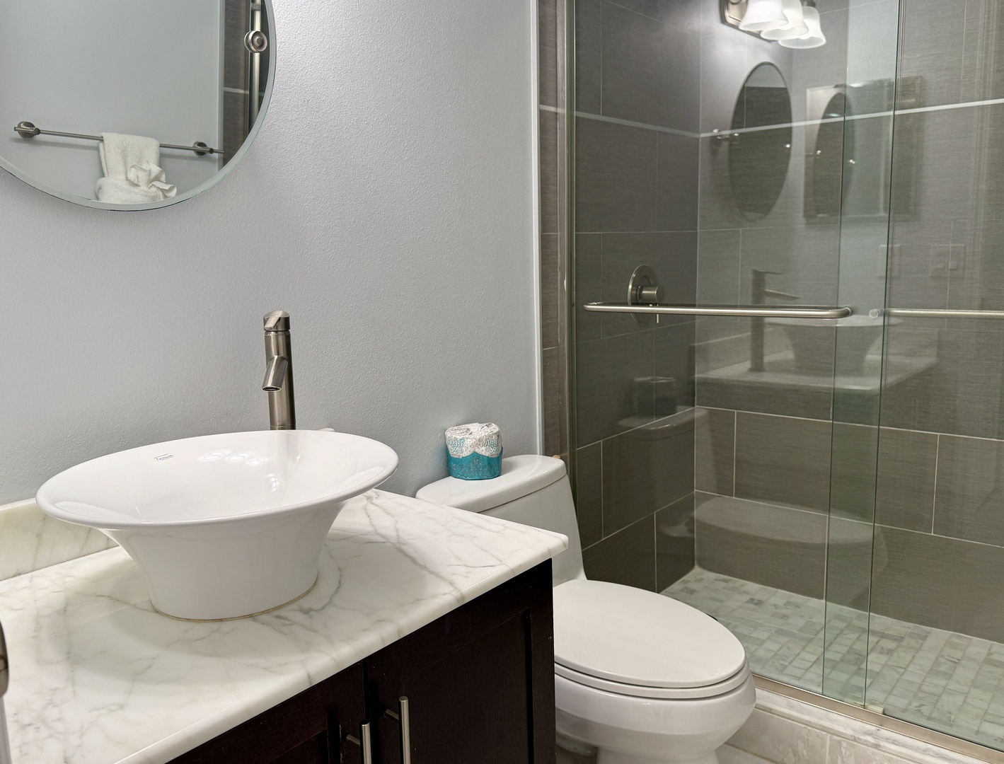 Step into your spa-like sanctuary with sleek marble counters, modern vessel sink, and spacious glass-enclosed shower with contemporary gray tile.