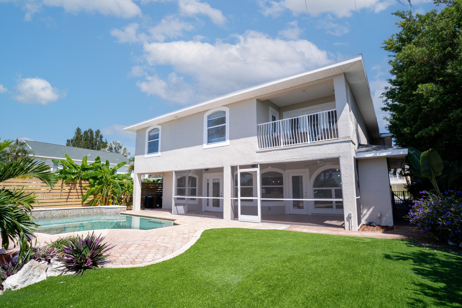 A modern two-story vacation home featuring a private swimming pool, manicured lawn, and tropical landscaping in a peaceful residential setting.