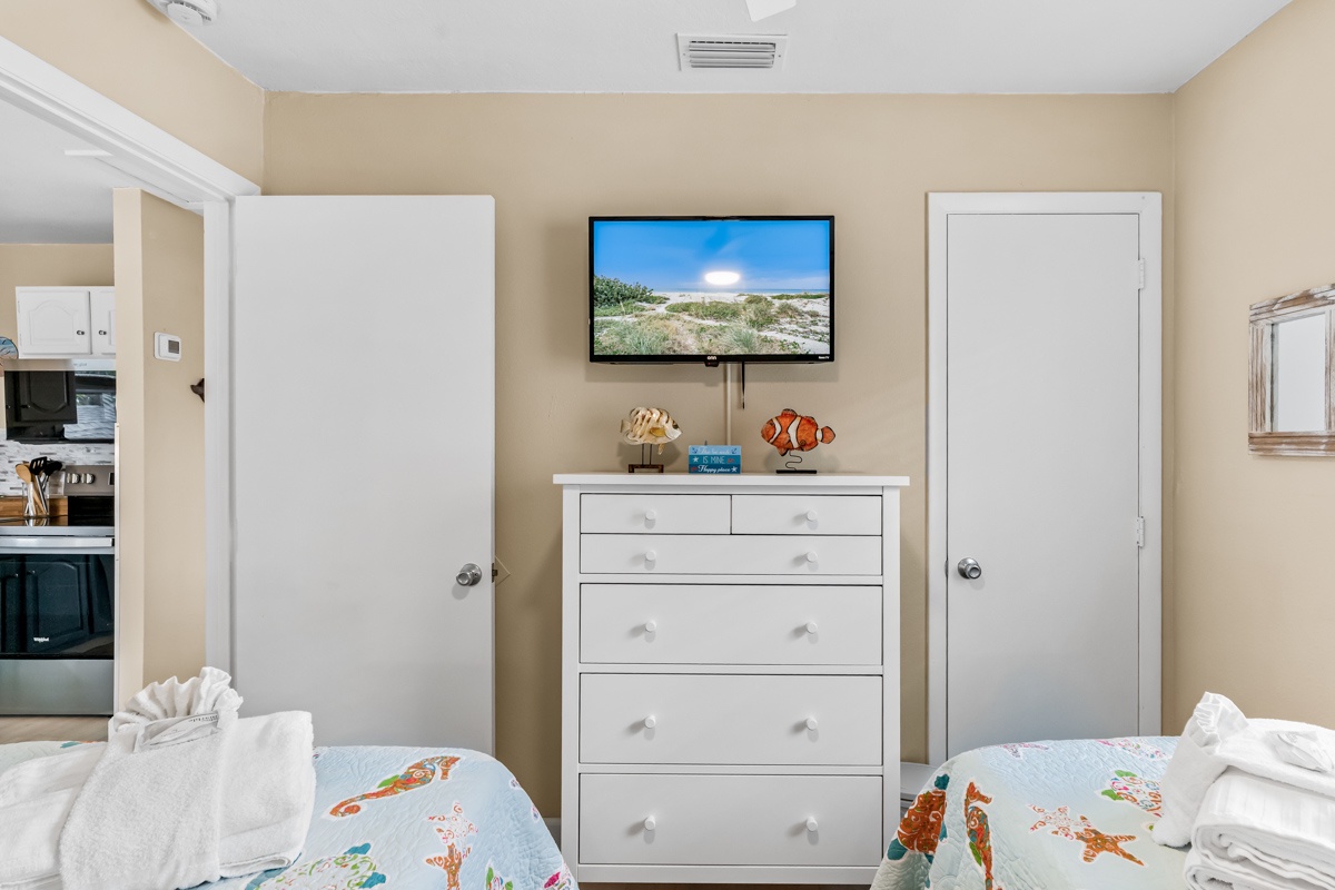Your comfortable bedroom features twin beds with playful sea-themed linens, wall-mounted TV, and plenty of storage in bright white drawers.