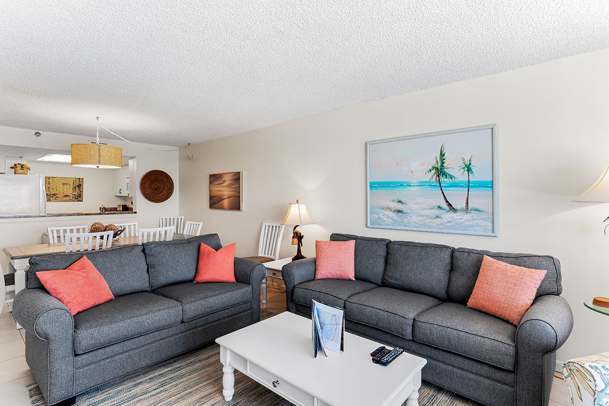 Sink into plush sofas with coral accents while beach art transports you to paradise. Your open living space flows seamlessly to the dining area.