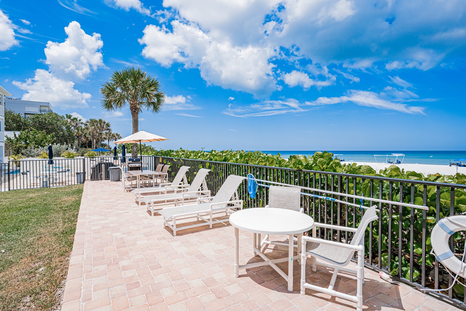 Beachfront patio overlooking turquoise waters with comfortable loungers and tropical landscaping perfect for relaxation and enjoying coastal breezes under sunny Florida skies.