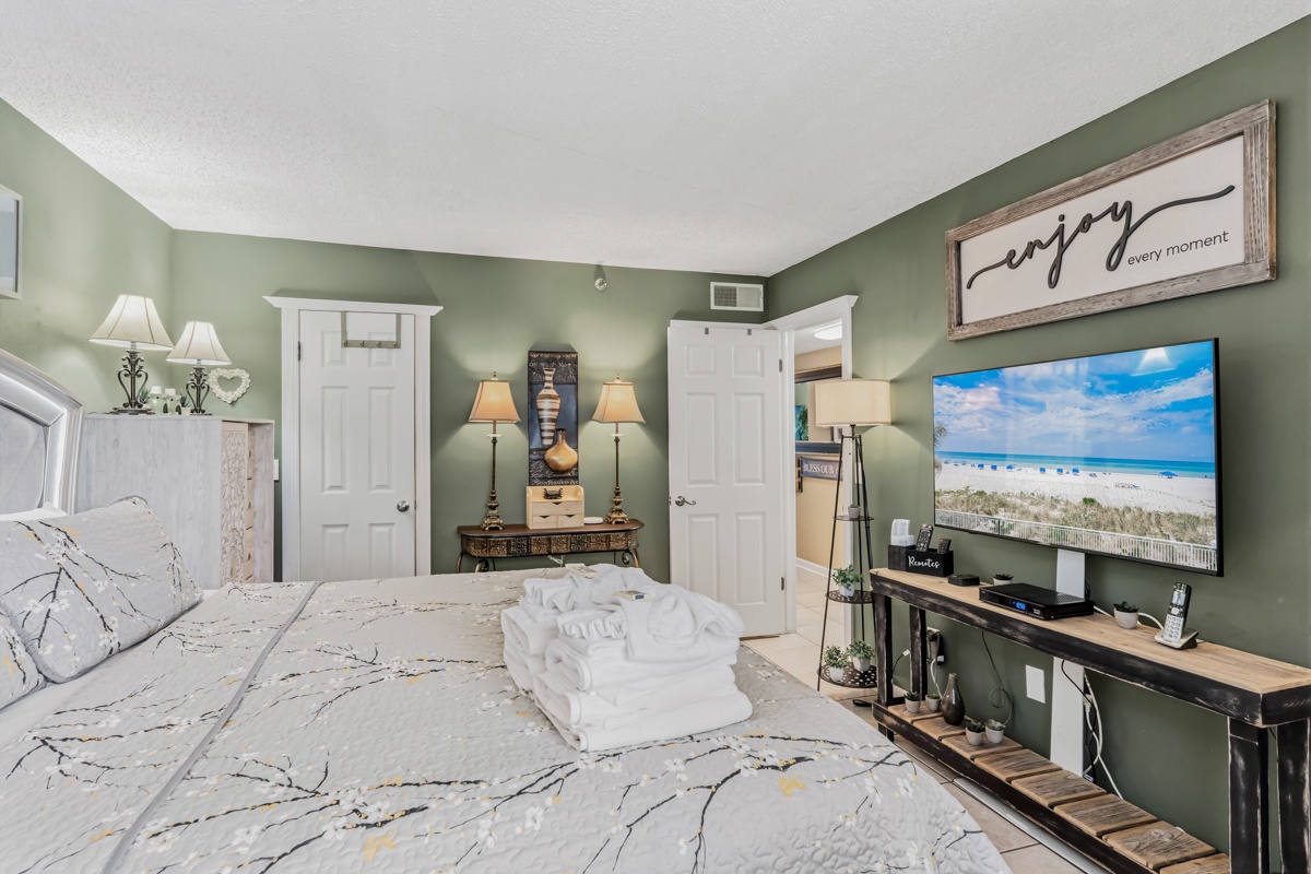 Unwind in your serene bedroom with calming sage walls, a plush bed, and a smart TV streaming coastal views—your peaceful retreat awaits.
