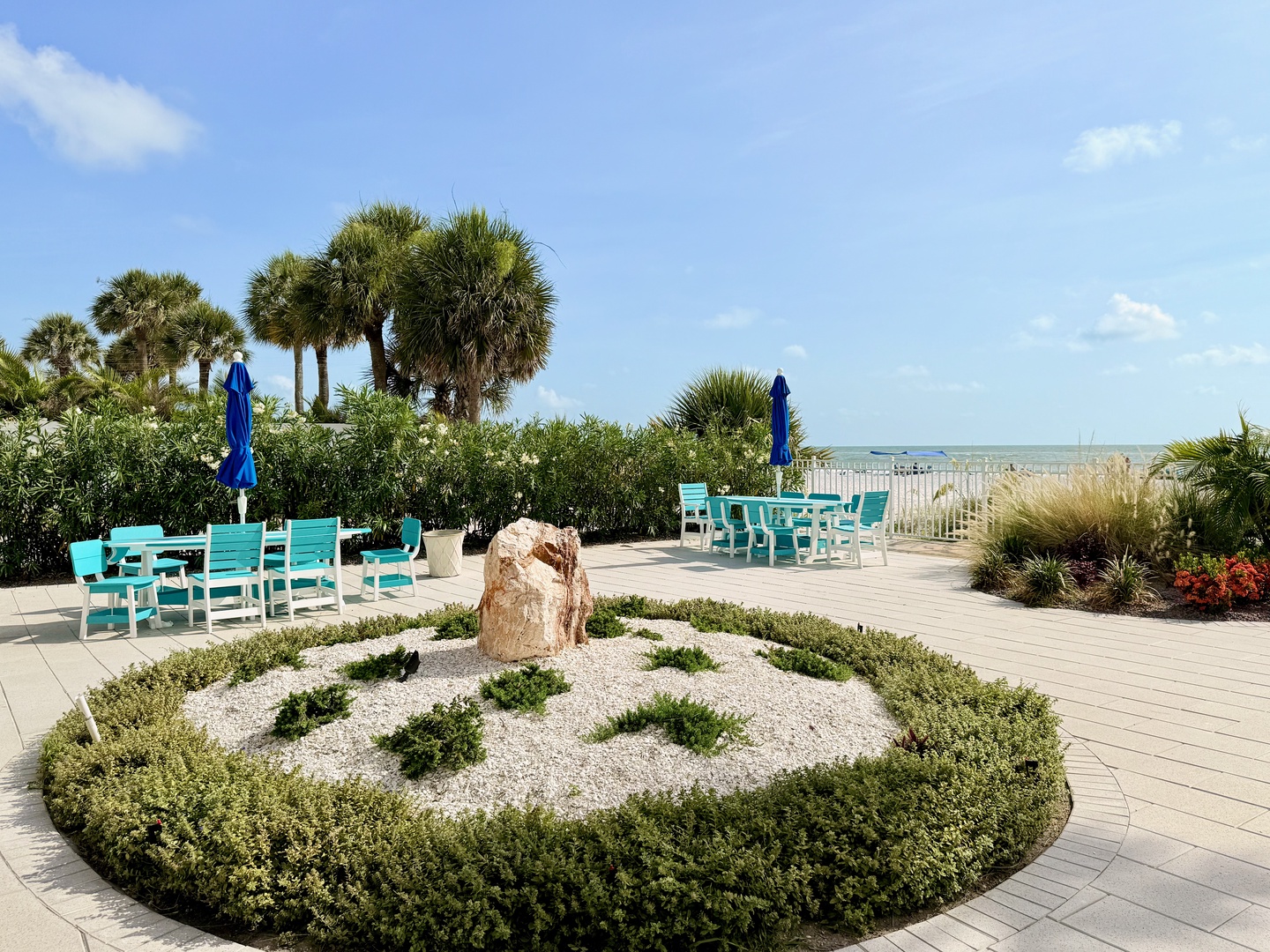 Coastal outdoor seating area framed by tropical palms and a thoughtfully designed garden centerpiece, with direct access to the sandy shoreline nearby.