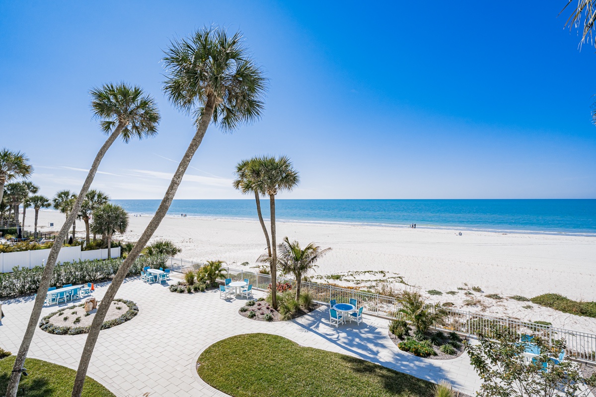 Beachfront property featuring pristine white sand, swaying palm trees, and direct access to crystal-clear turquoise waters with inviting lounge seating along the shore.
