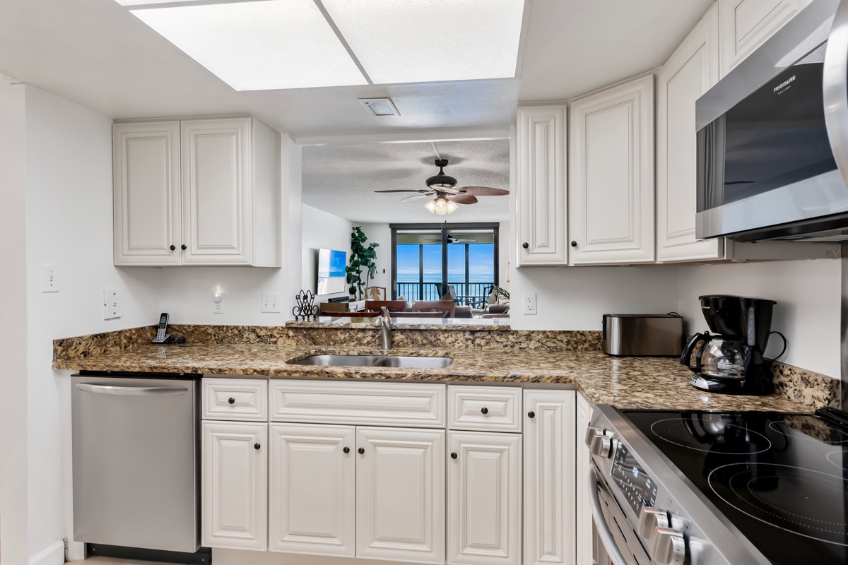 Prepare your meals in this bright, fully-equipped kitchen featuring granite countertops and modern appliances—with natural light flooding in from the skylight above and ocean views glimpsed through the living area beyond.