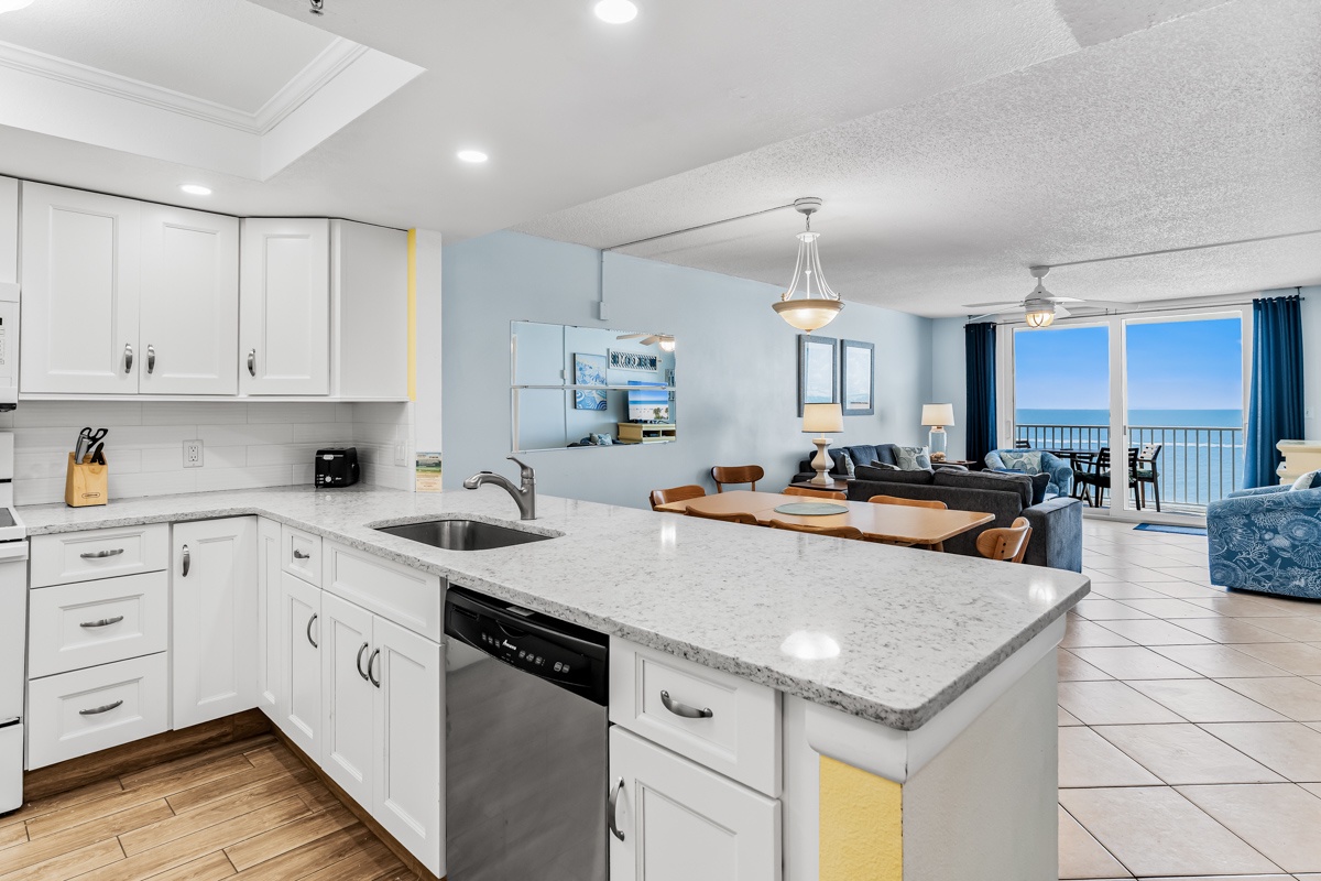 Imagine yourself preparing meals in this bright, fully-equipped kitchen with ocean views beckoning beyond. Crisp white cabinetry and modern appliances make cooking a breeze while your gathering unfolds in the open, airy space.
