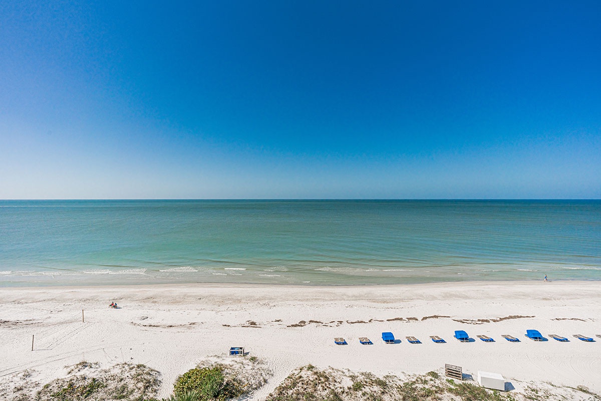 Beautiful beach with white sand, turquoise waters, and organized beach chairs under clear blue skies.