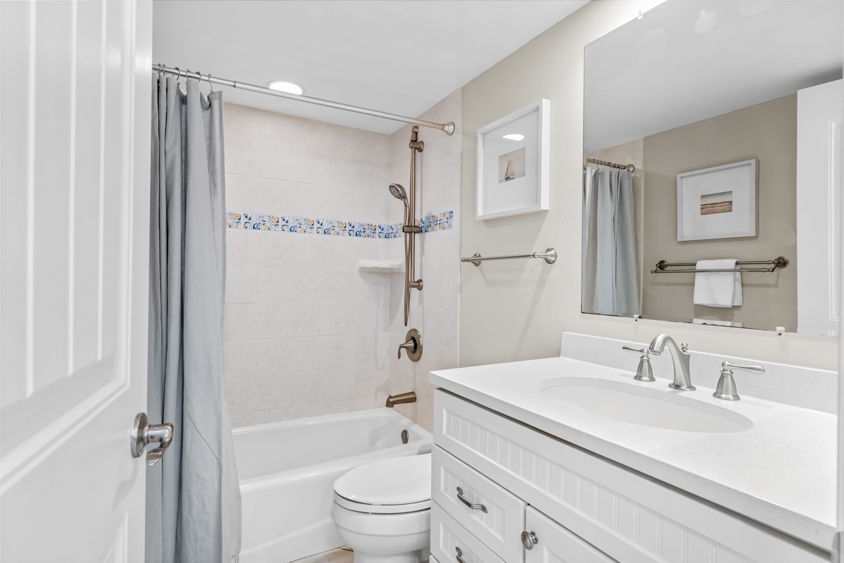Hallway bathroom featuring a tub-shower combo with charming mosaic tile accents and elegant vanity with ample counter space.