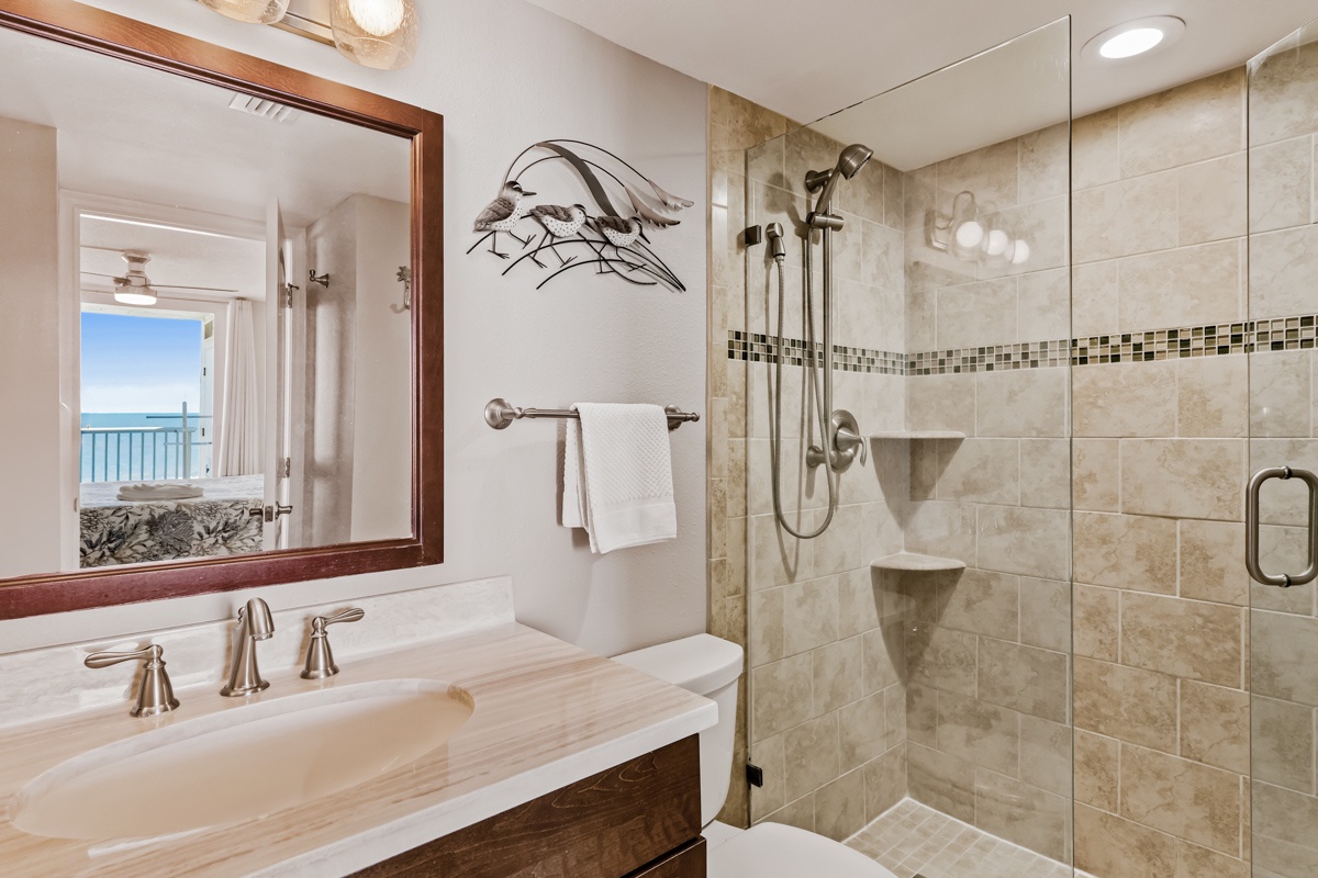 Unwind in your luxurious bathroom featuring a rainfall shower, stone vanity top, and coastal artwork—all with stunning ocean views just steps away.