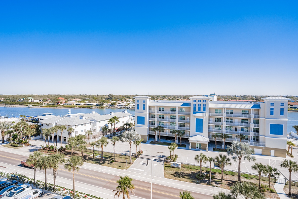 Modern waterfront resort complex featuring contemporary architecture with blue accents, surrounded by palm trees and coastal views.