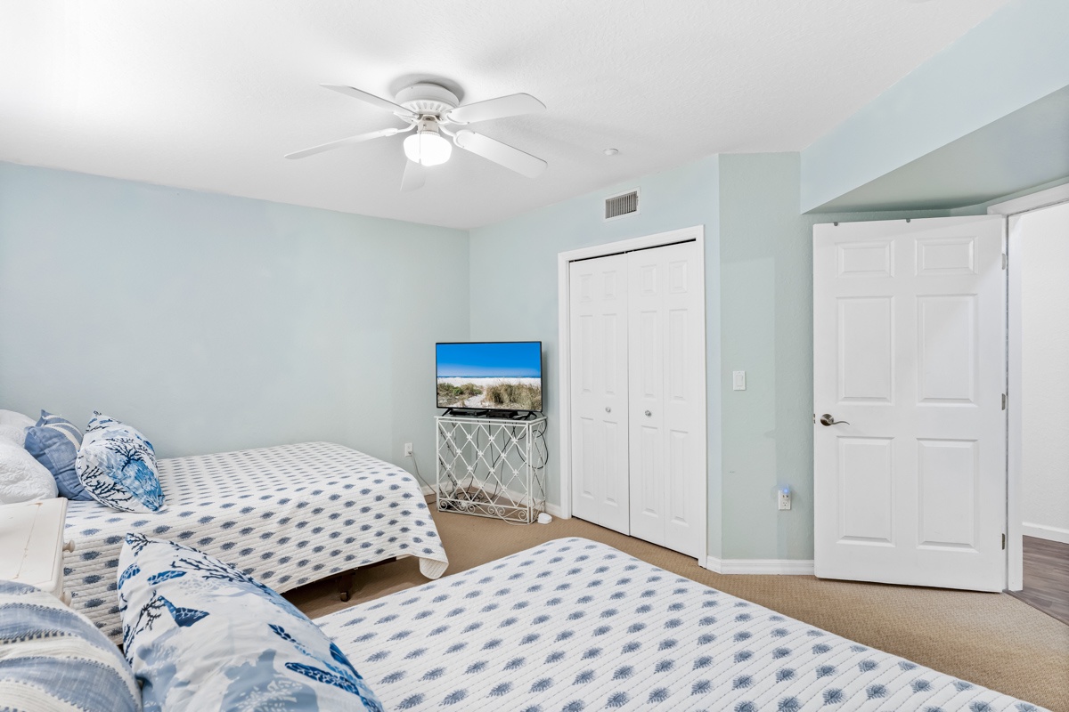 Unwind in your serene twin bedroom with soft blue accents, ceiling fan for comfort, and flat-screen TV for relaxation.
