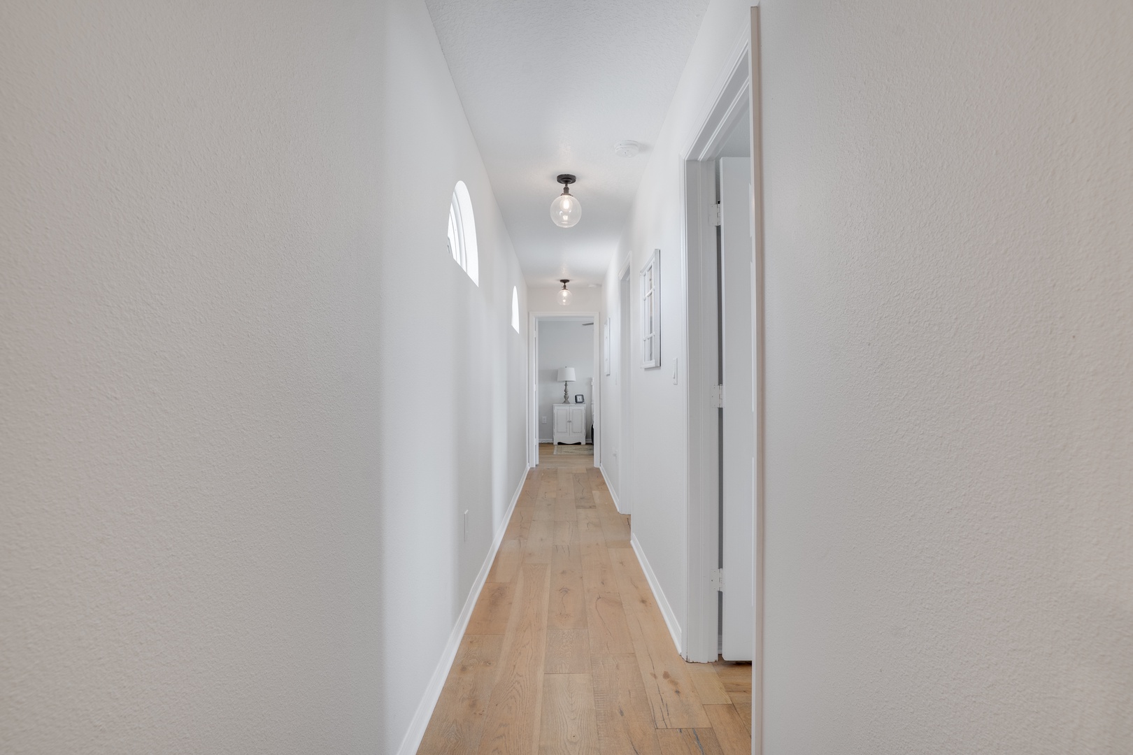 Walk through this bright, welcoming hallway with warm wood floors and elegant pendant lighting leading to your private spaces.
